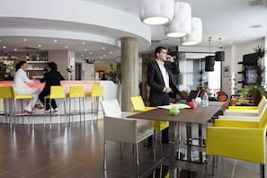 A modern hotel lobby with a reception desk, yellow and white seating, and a large table with a laptop. - Novotel Suites Malaga Centro (Málaga)