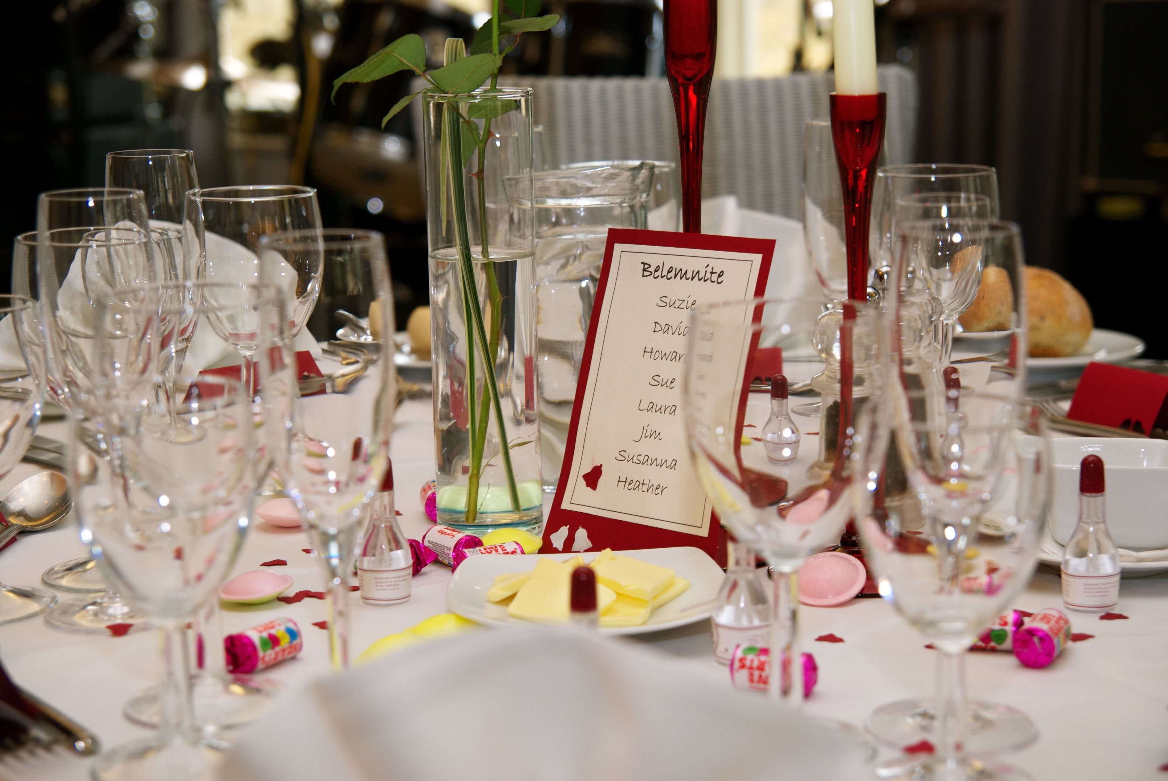A table set for a formal event with empty wine glasses, a menu sign, and scattered rose petals.