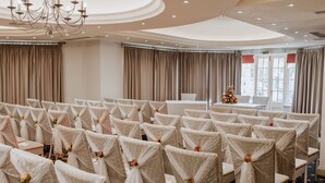 Un salón de banquetes con filas de sillas cubiertas de tela blanca y atadas con cintas, una araña y un árbol de Navidad.