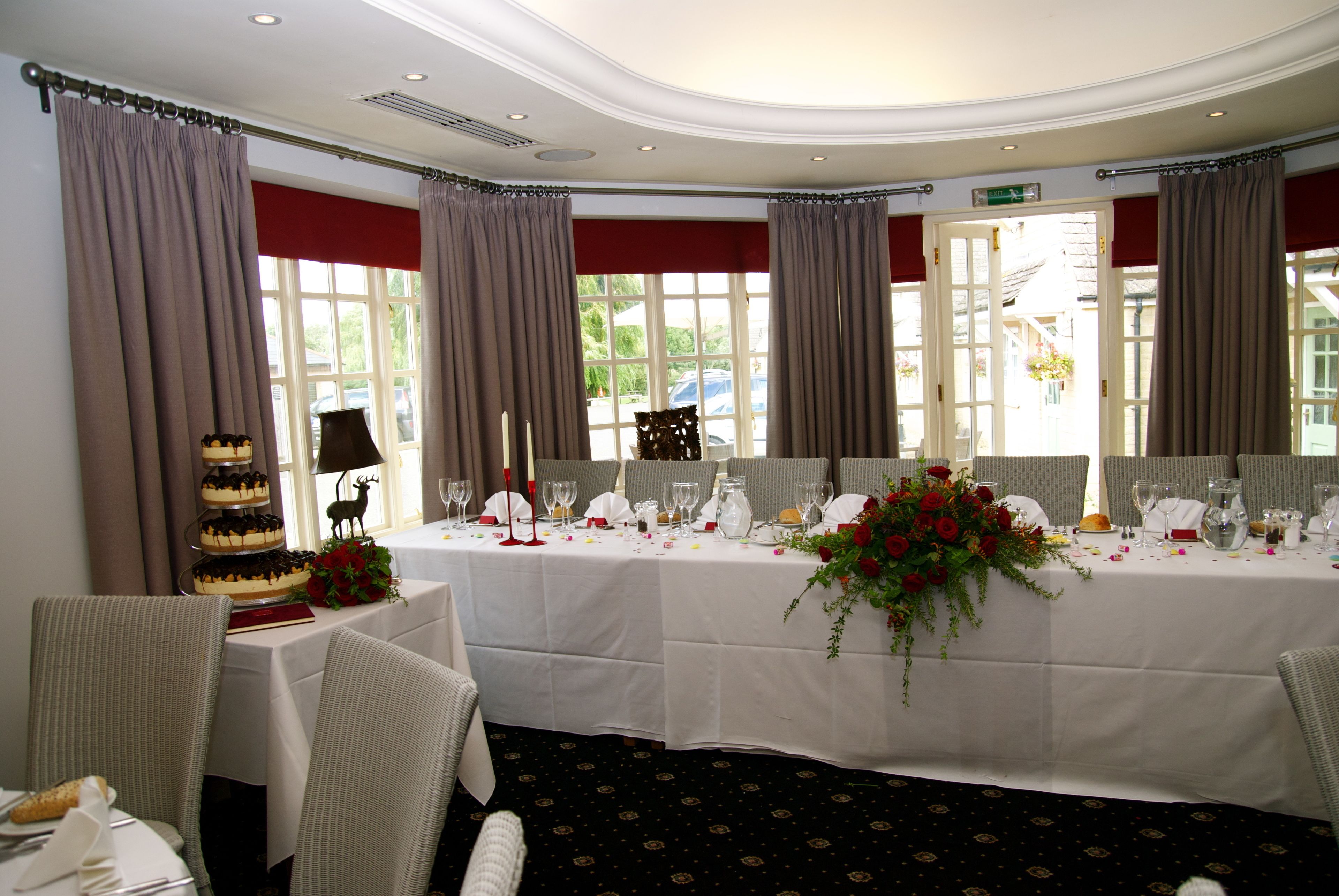 A banquet hall with a white tablecloth, floral centerpiece, and a tiered cake.
