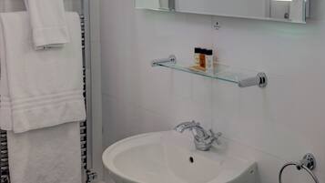 A bathroom with a white sink, a glass shelf with toiletries, and a towel rack.