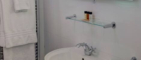 Un baño con un lavabo blanco, un estante de vidrio con artículos de aseo y un perchero para toallas.