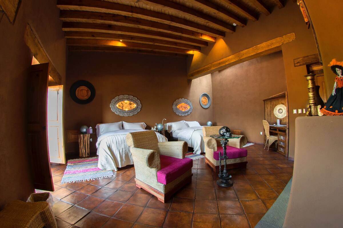 Une pièce confortable avec un lit, deux fauteuils en osier, une petite table et une lampe décorative.