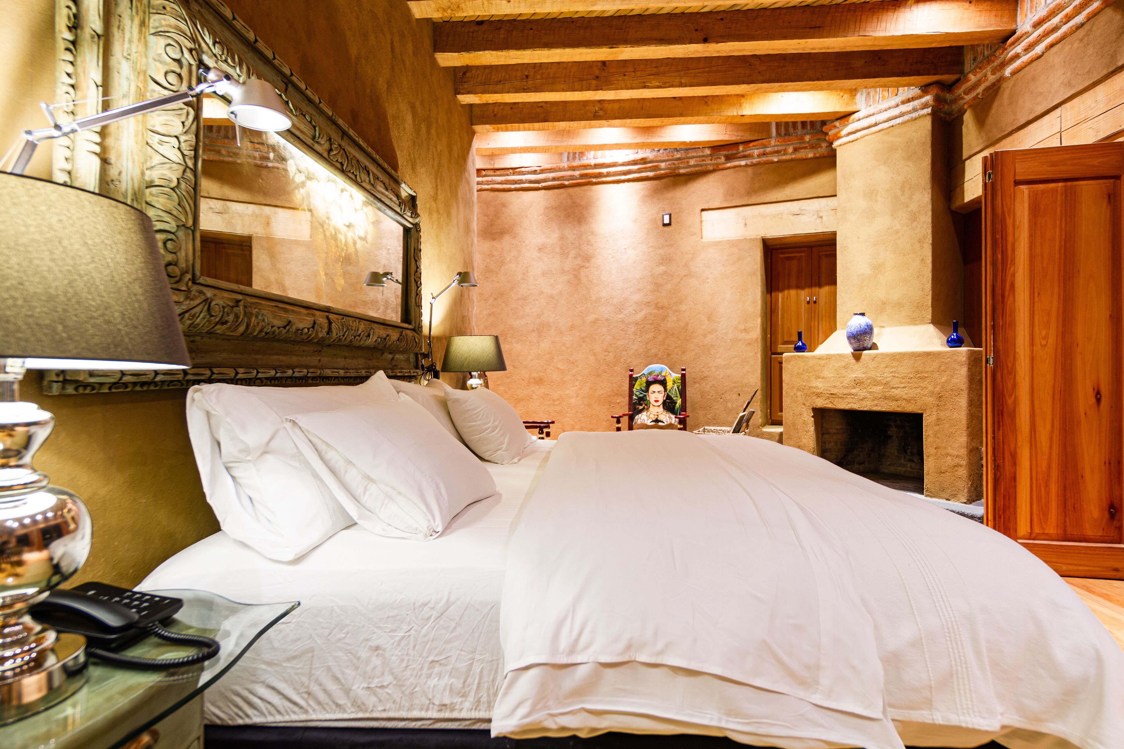 Habitación de hotel con cama, lámparas de noche, un espejo, chimenea y puerta de madera.