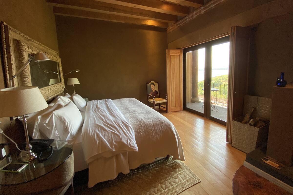Une chambre avec un grand lit, un bureau avec une lampe, une chaise et une vue sur l’extérieur grâce à une porte vitrée.