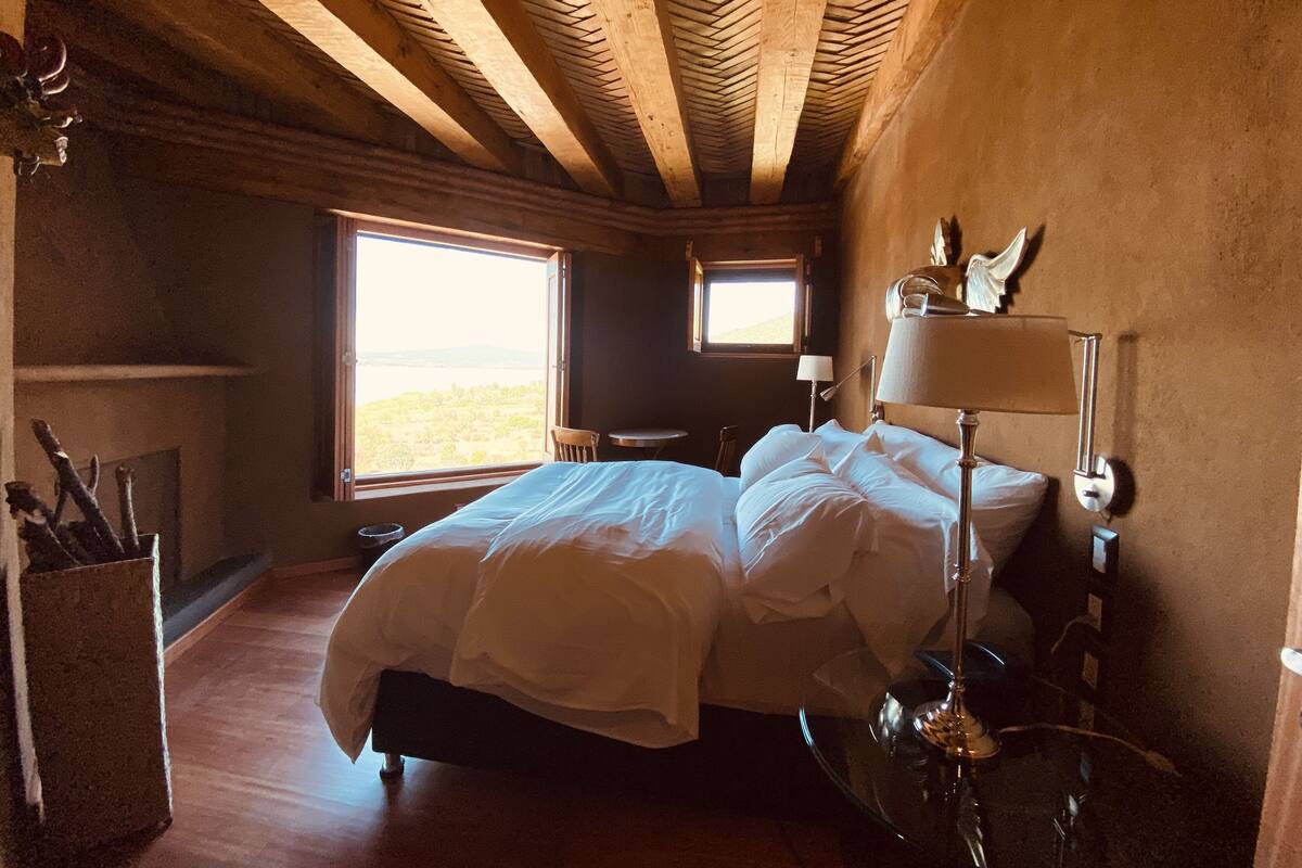 Une chambre avec un plafond en bois, un lit, une table de chevet avec une lampe et une fenêtre donnant sur l’extérieur.