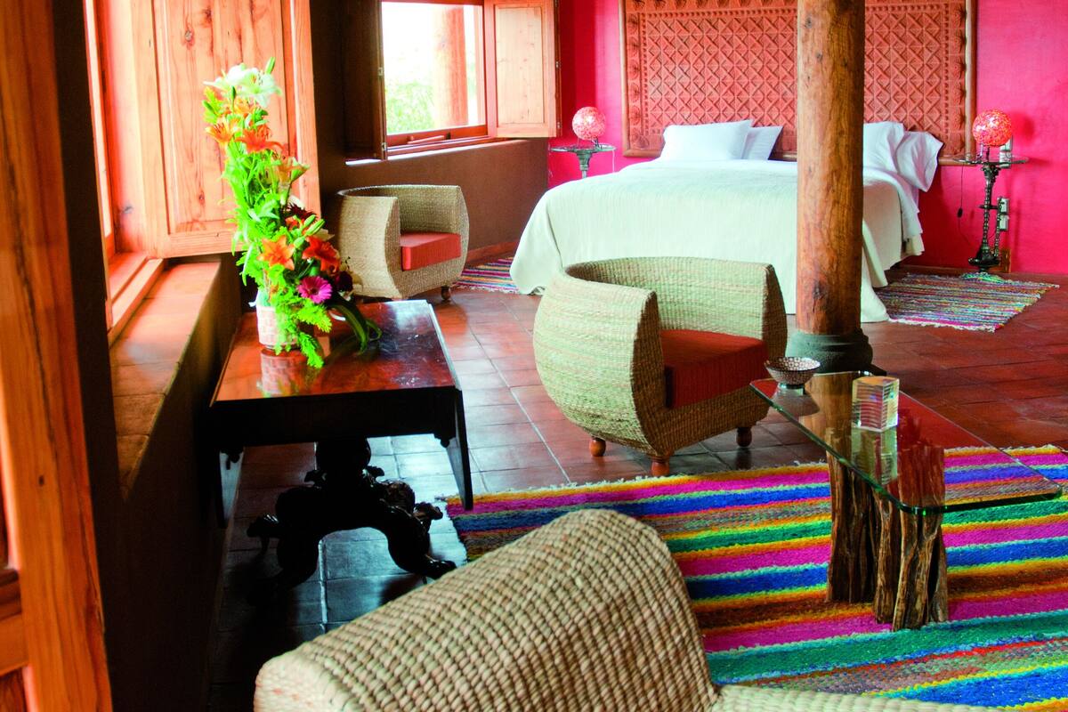 Une pièce avec un lit, une chaise, une table ornée d’un vase et une fenêtre.
