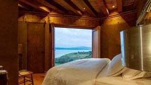 Ein Schlafzimmer mit einem großen Bett, Holzbalkendecke und Blick auf einen See und Hügel.