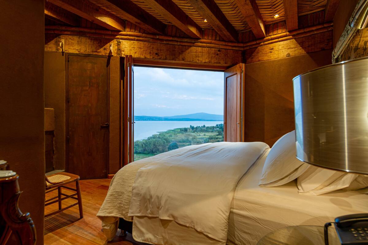 Une chambre avec un grand lit, un plafond en bois et une vue sur un lac et des collines.