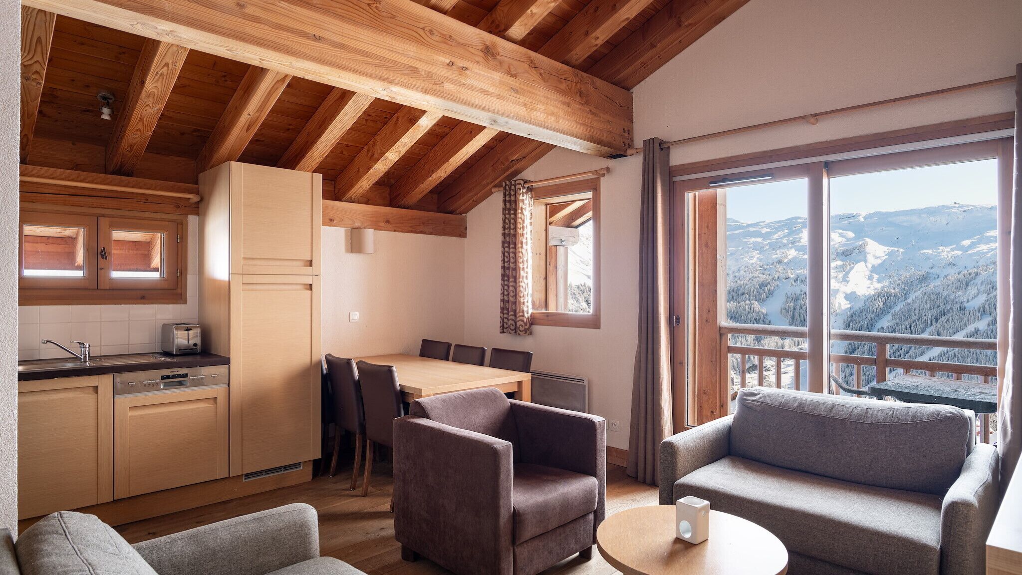 A cozy cabin with a wooden interior, a dining area, and a large window offering a mountain view.