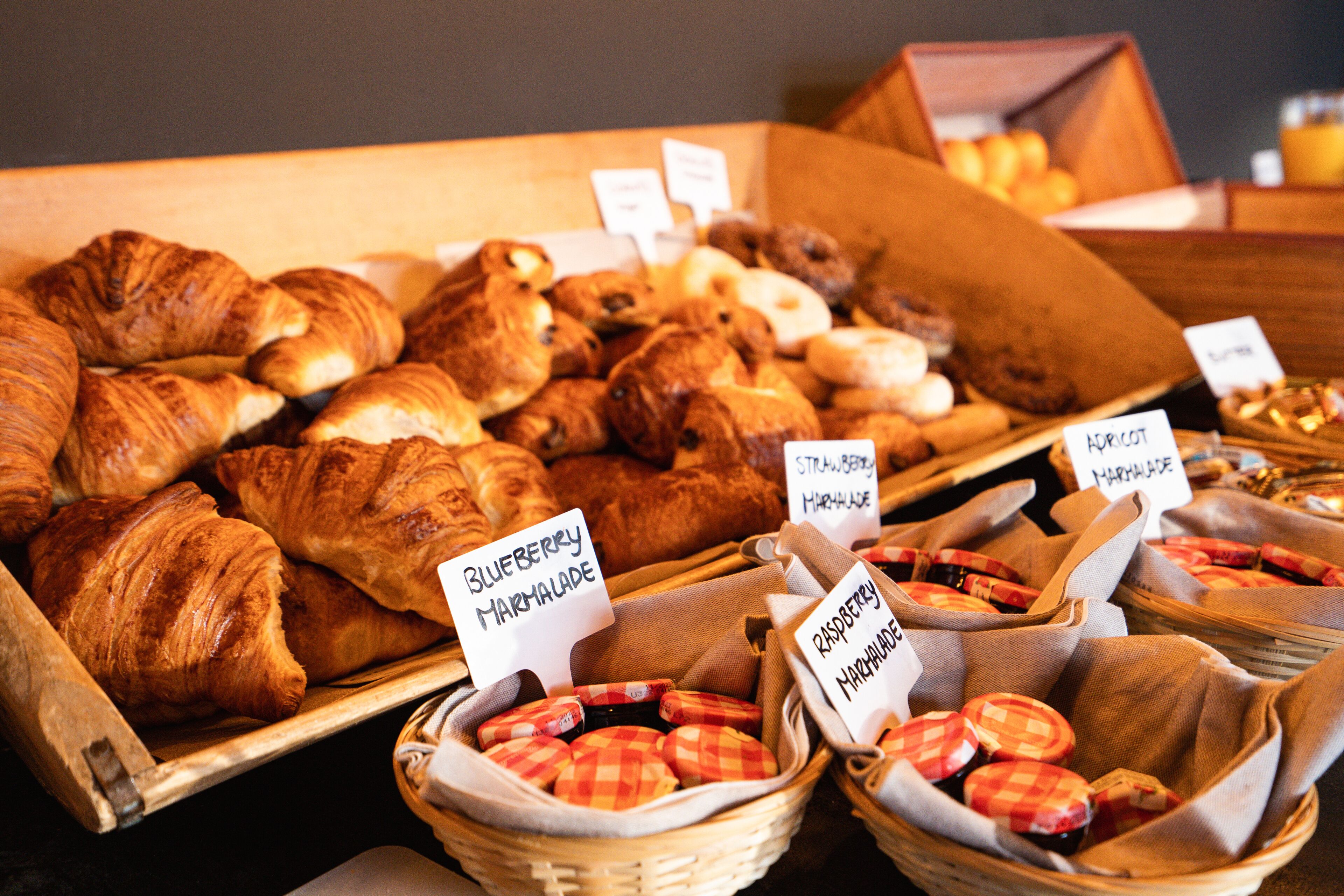 Diverse gebakjes en broodjes gepresenteerd in manden en houten dienbladen, met labels die smaken aangeven zoals bosbes en framboos.