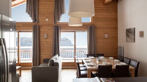 A dining area with a wooden table set for four, a sofa, and a large window with curtains. - Dormio Resort Les Portes du Grand Massif (Araches-la-Frasse)