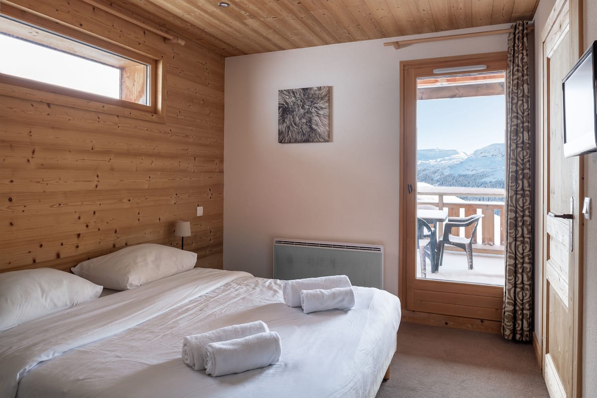 A wooden-paneled room with a bed, a radiator, and a view of mountains through a door.