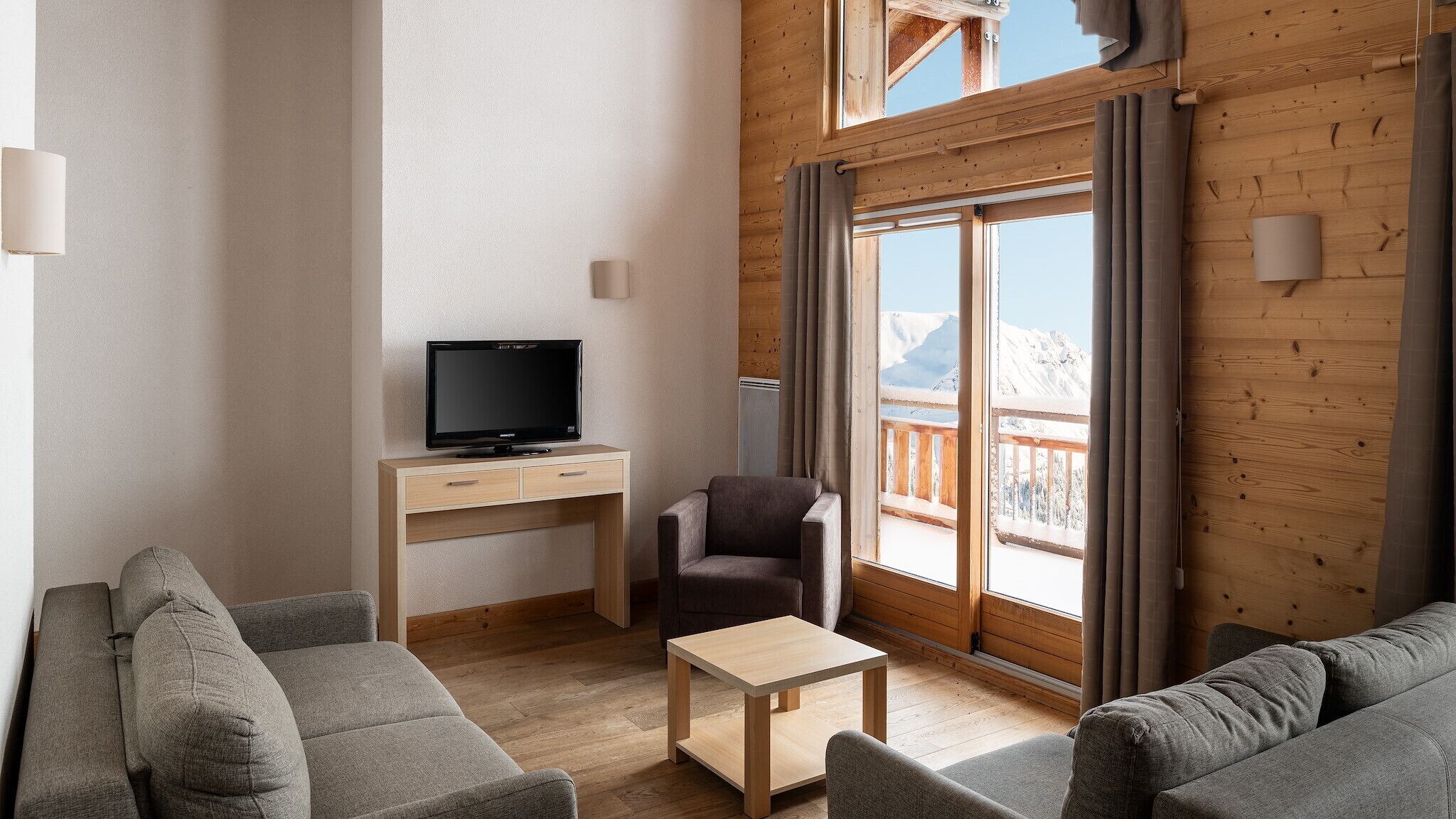 A modern living room with a flat-screen TV, a sofa, a chair, and a small table.