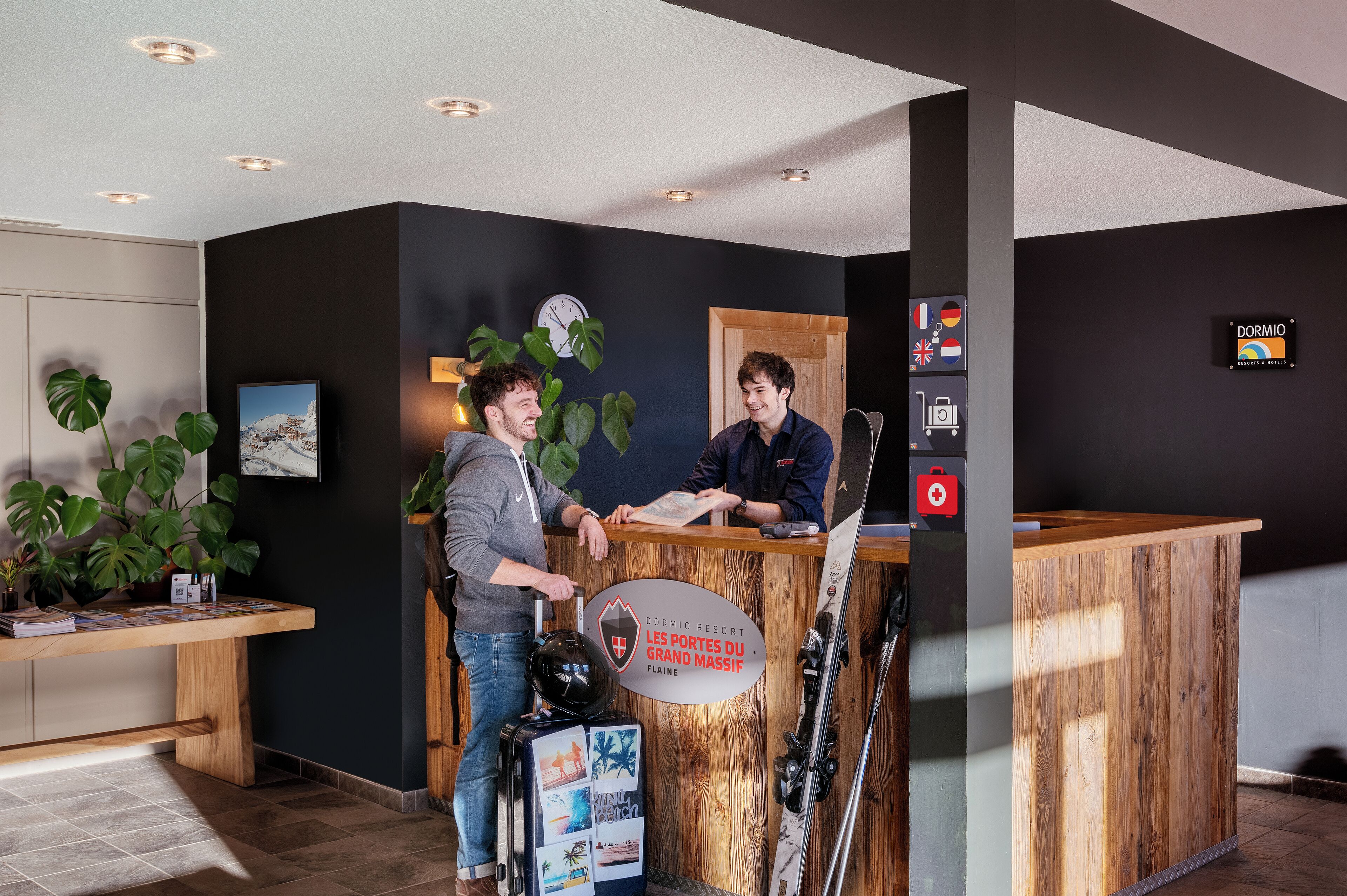 A reception desk at a hotel with a wooden finish, a clock, and a sign indicating it's a resort in Falaise.