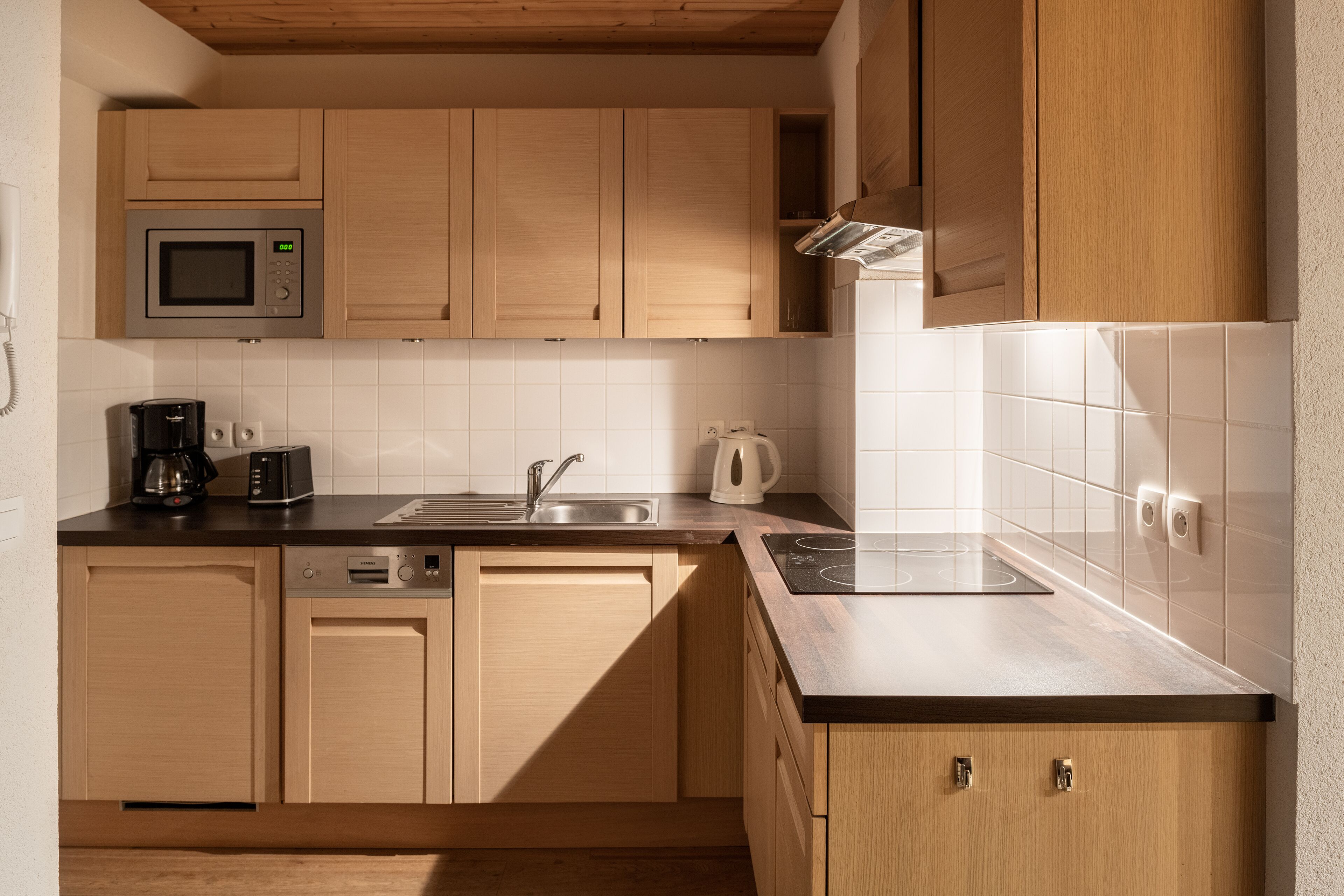 A modern kitchen with wooden cabinets, a microwave, a coffee maker, and a kettle.
