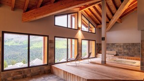A spa area with wooden flooring, a hot tub, and large windows offering a view of a forested landscape. - Dormio Resort Les Portes du Grand Massif (Araches-la-Frasse)
