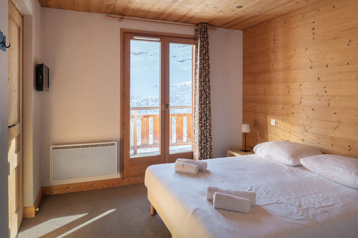 A bedroom with a bed, a heater, a TV, and a view of snowy mountains through a door.