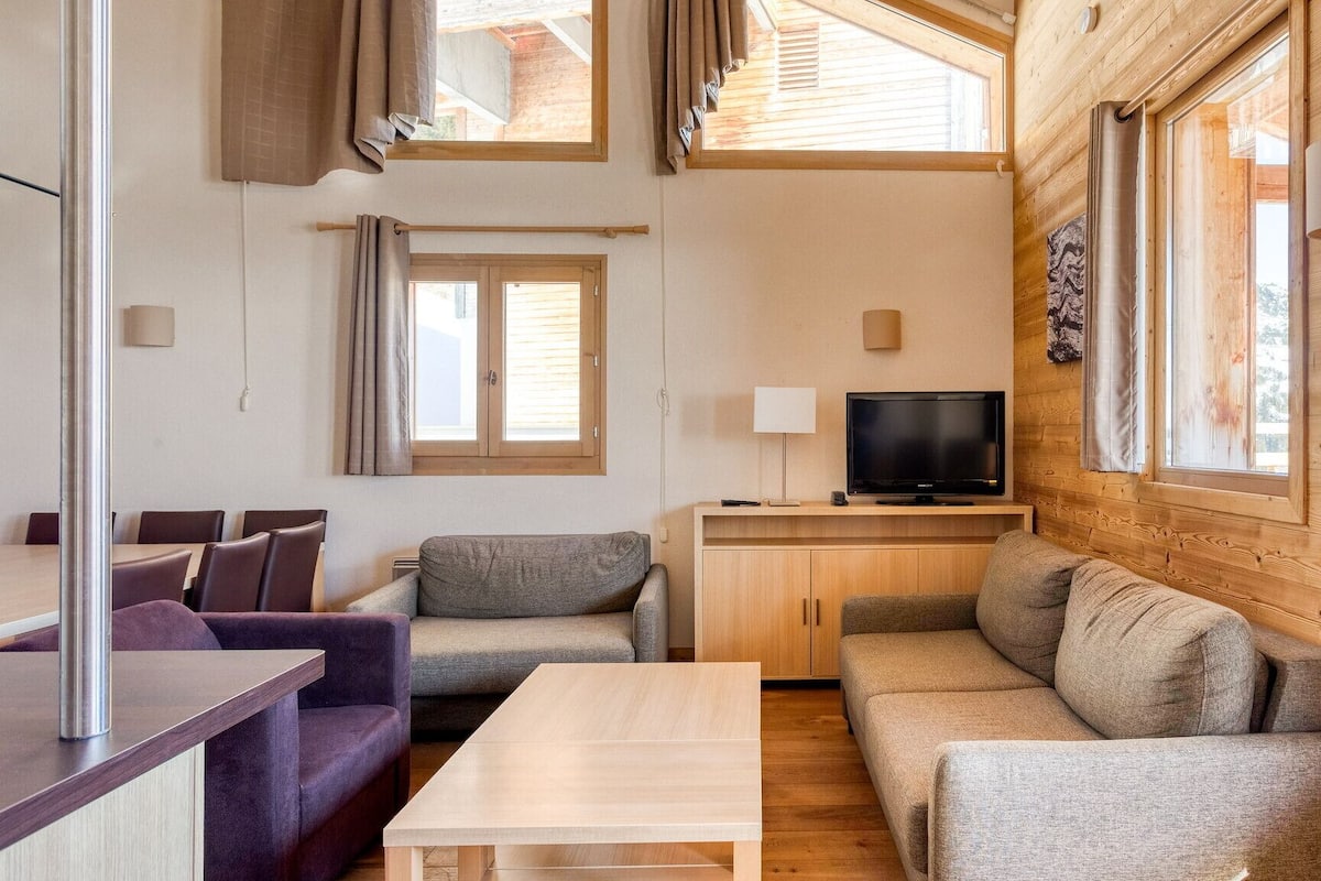 A cozy cabin interior with a wooden interior, a sofa, a TV, and a dining area.