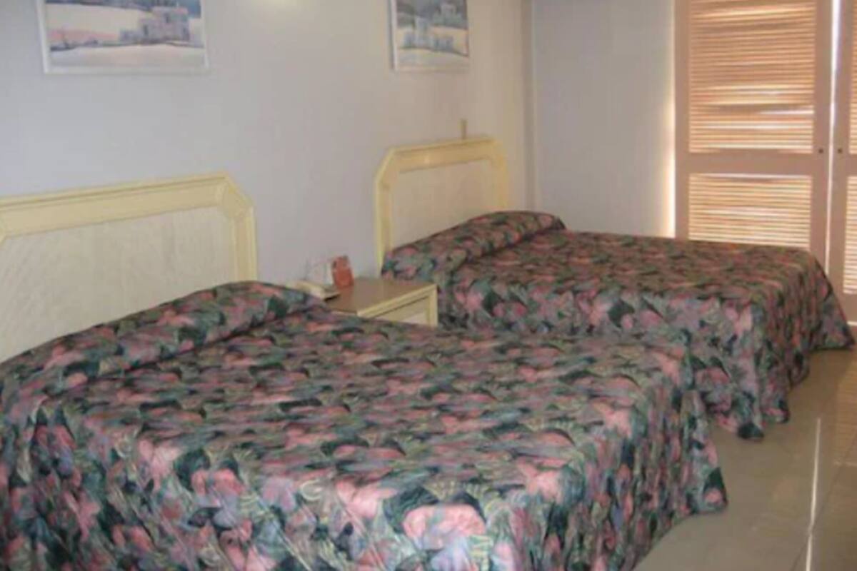 A bedroom with two single beds, a nightstand, and a window with blinds.