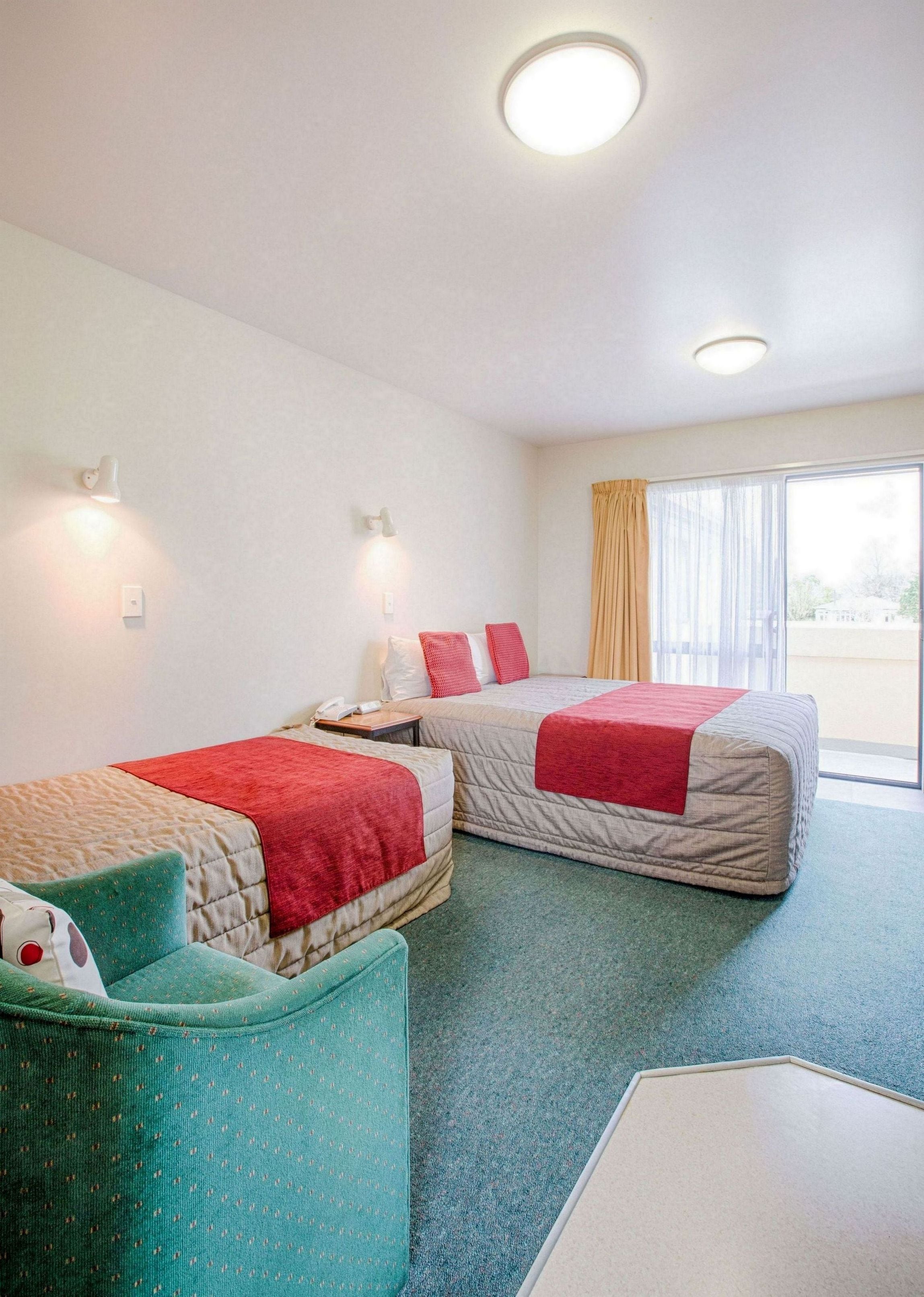 A hotel room with two beds, a small sofa, a desk, and a window with curtains.