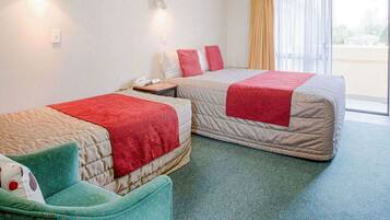 Een hotelkamer met twee bedden, een kleine zithoek, een bureau en een raam met gordijnen.
