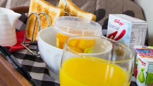 A breakfast tray with toast, orange juice, and a bowl of cereal on a checkered tablecloth.