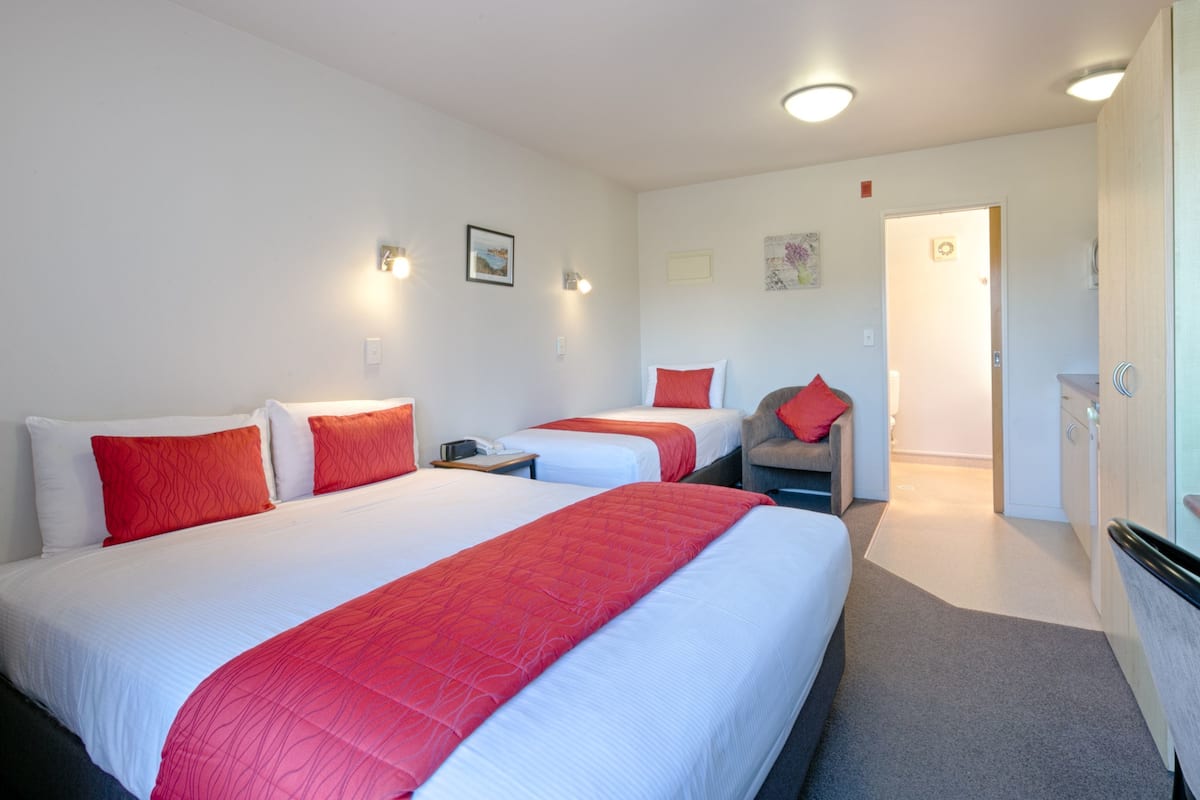 A hotel room with two beds, each with red and white bedding, a small desk, a chair, and a door leading to a bathroom.