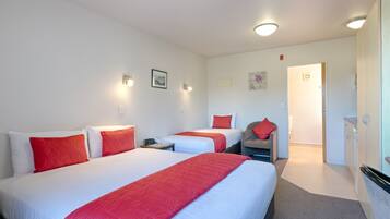 A hotel room with two beds, each with red and white bedding, a small desk, a chair, and a door leading to a bathroom.