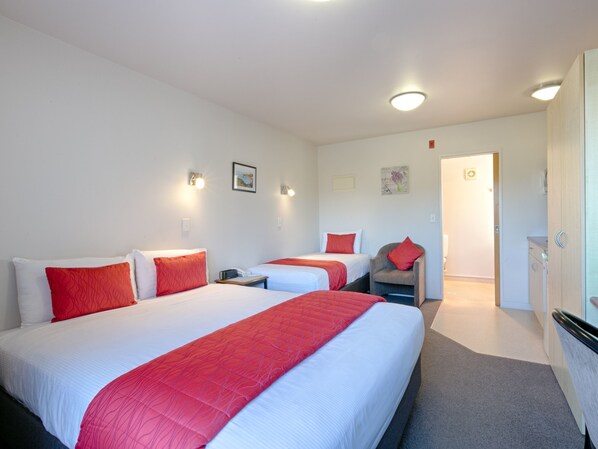Habitación de hotel con dos camas, cada una con ropa de cama roja y blanca, un escritorio pequeño, una silla y una puerta que da a un baño.
