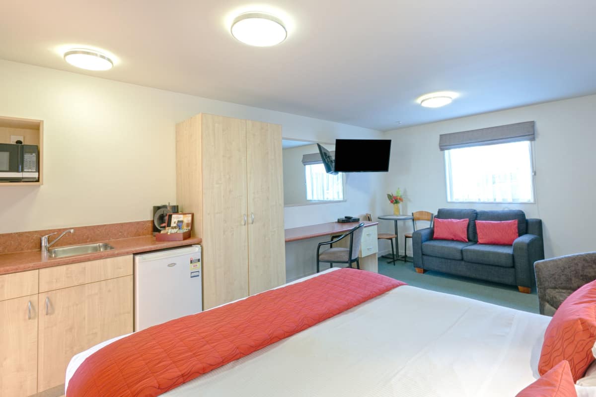 A hotel room with a bed, a desk, a sofa, a TV, and a kitchenette.
