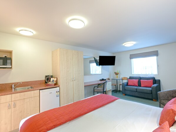 A hotel room with a bed, a desk, a sofa, a TV, and a kitchenette.