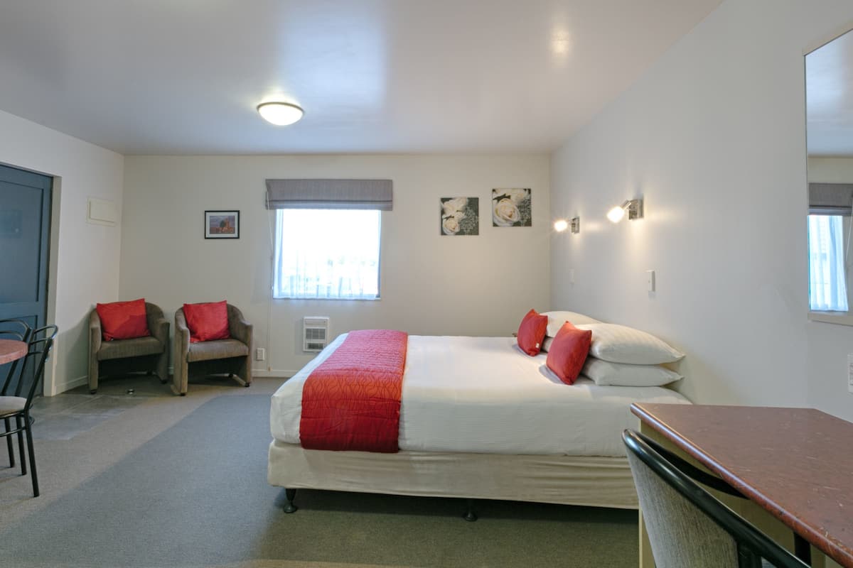 A hotel room with a bed, two chairs, a desk, and a window.