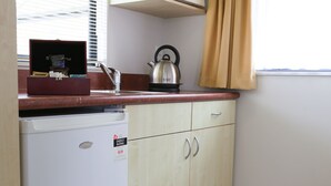A compact kitchen with a white refrigerator, a microwave, a kettle, and wooden cabinets.