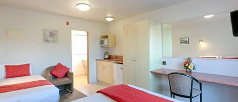 Habitación de hotel con dos camas, un escritorio, una silla, kitchenette y baño.
