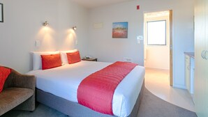 A hotel room with a large bed, a bedside table, a chair, and a door leading to the bathroom.