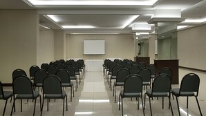 Un salón de conferencias con filas de sillas orientadas hacia una pizarra, un atril y un espejo grande en la pared.