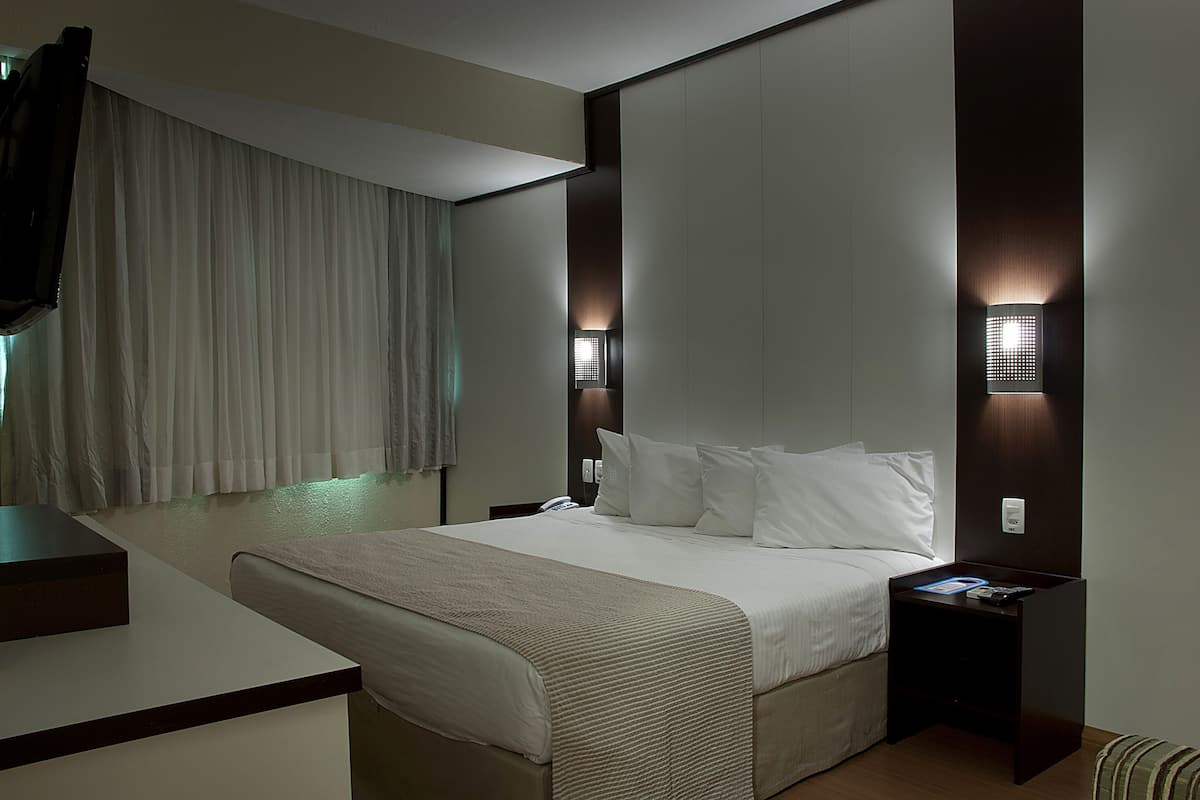 A modern hotel room with a large bed, bedside tables, and a TV mounted on the wall.