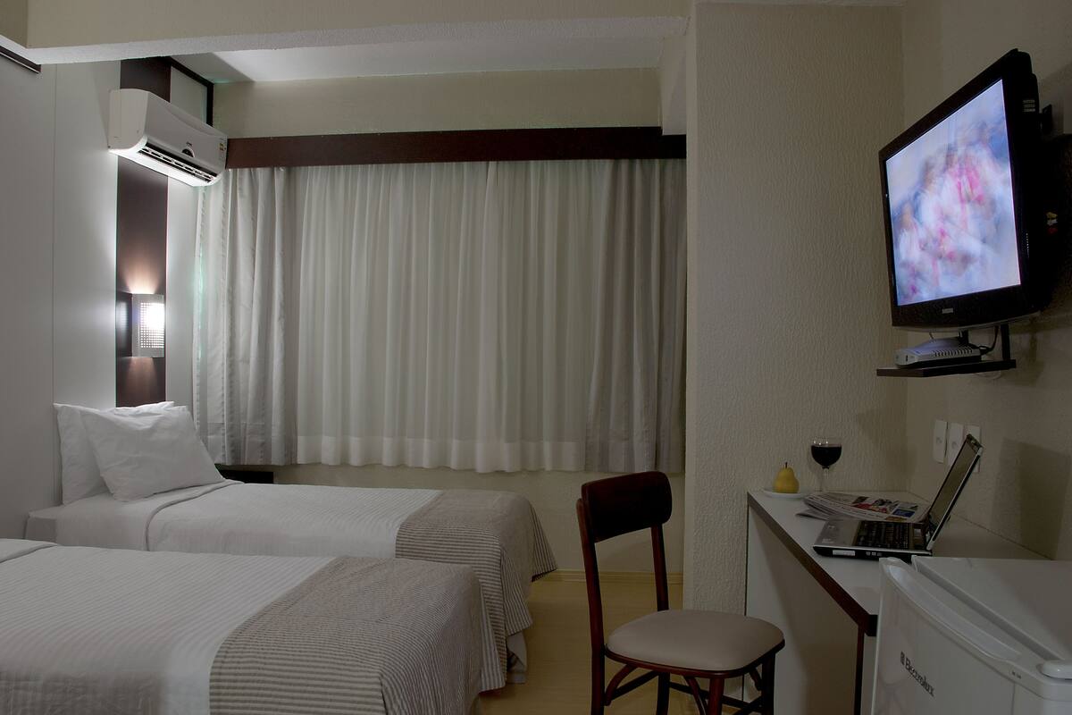 A hotel room with two beds, a desk with a laptop and a wine glass, a television, and a chair.