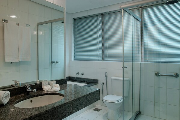 A modern bathroom with a granite sink, white toilet, and a glass shower enclosure.