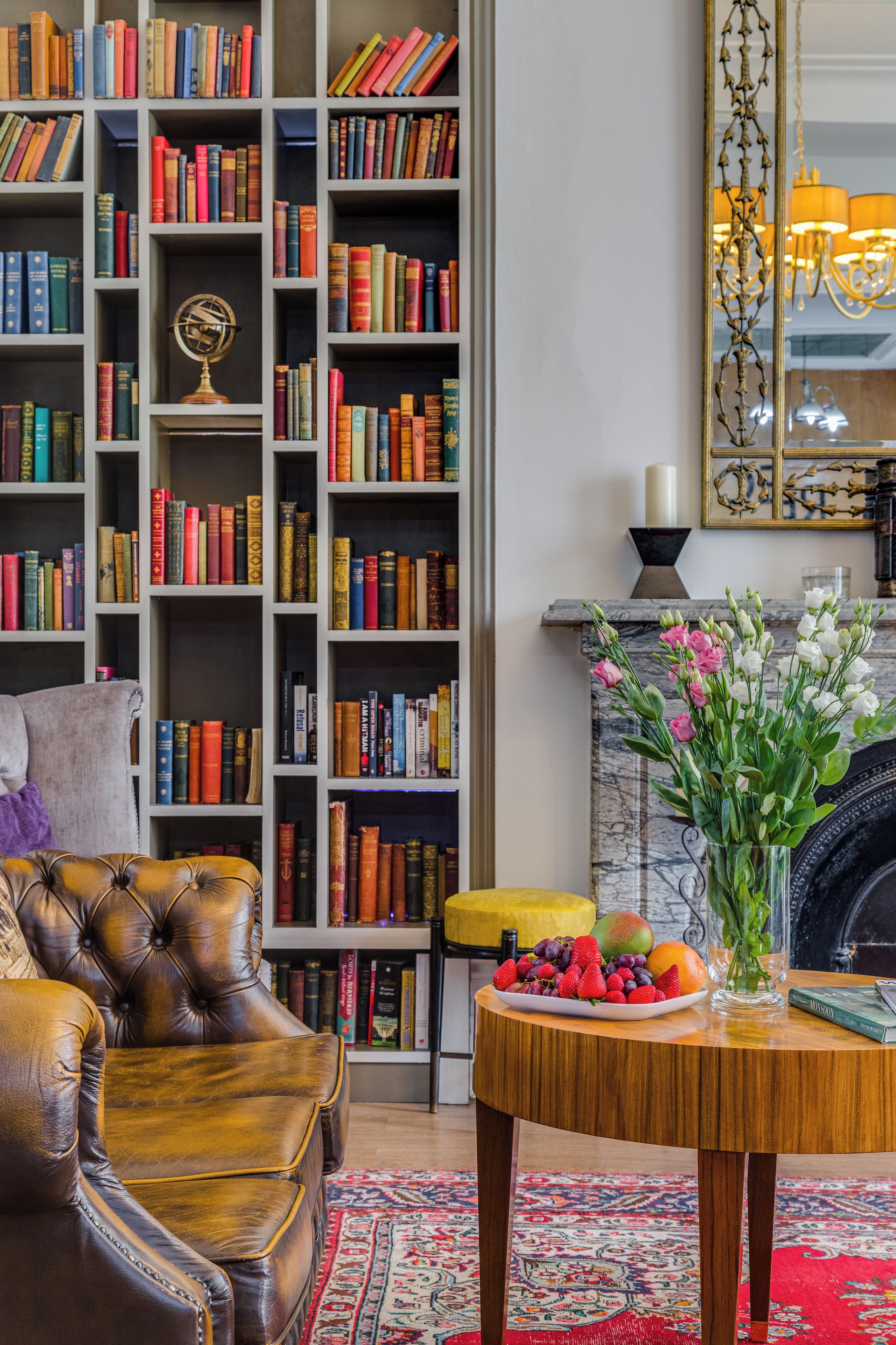 A library with a leather armchair, a wooden table with fruit, and a fireplace.