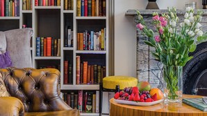 A library with a leather armchair, a wooden table with fruit, and a fireplace. - 1 Lexham Gardens (London)