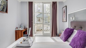 A hotel room with a bed, a desk, a chair, a window with curtains, and a view of a building outside. - 1 Lexham Gardens (London)