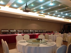A conference room with round tables, white chairs, and a buffet line with food containers. - Shenzhen New Times Hotel (Shenzhen)