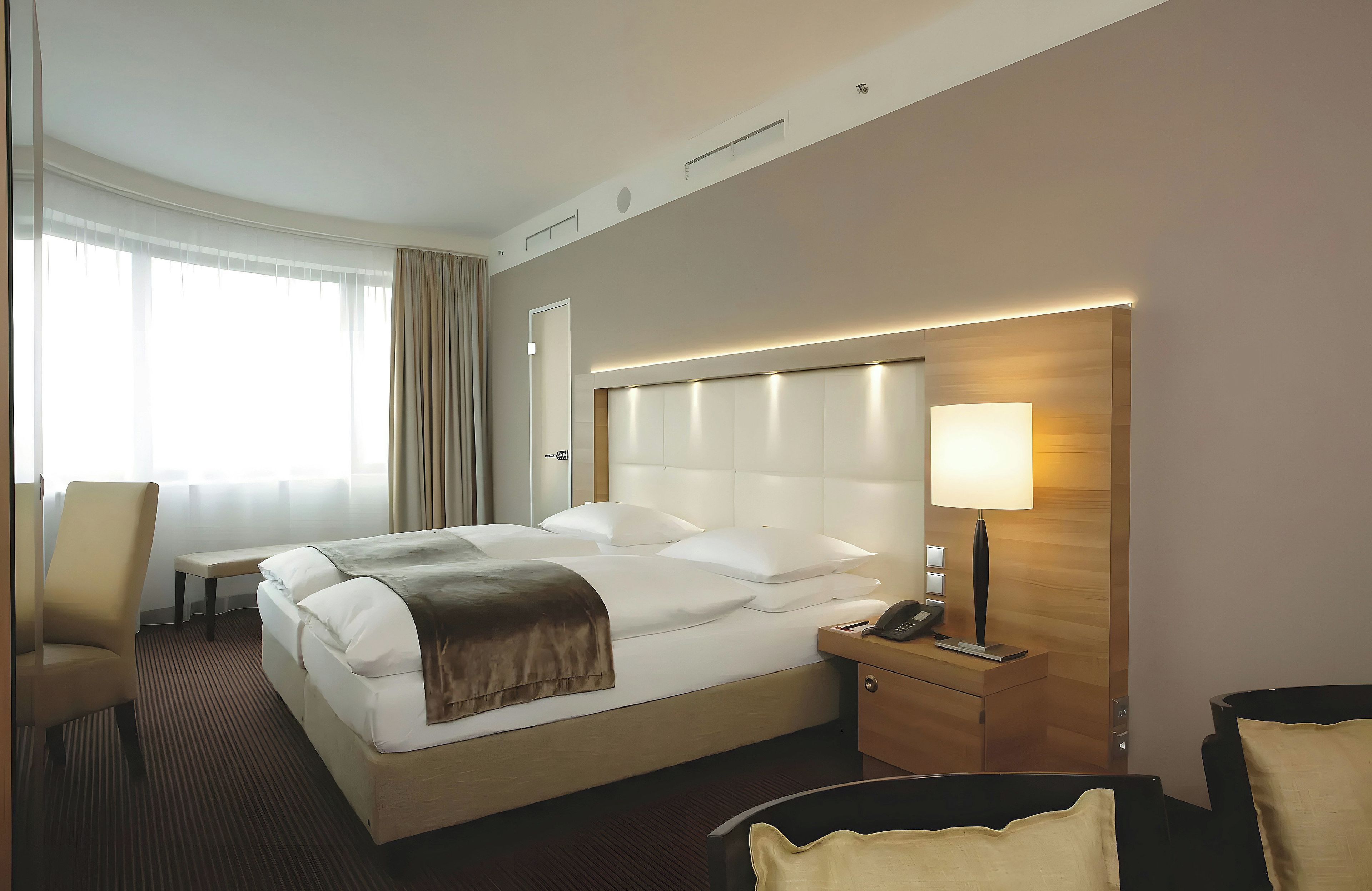 Una habitación de hotel con cama, mesita de noche, lámpara, silla y escritorio.