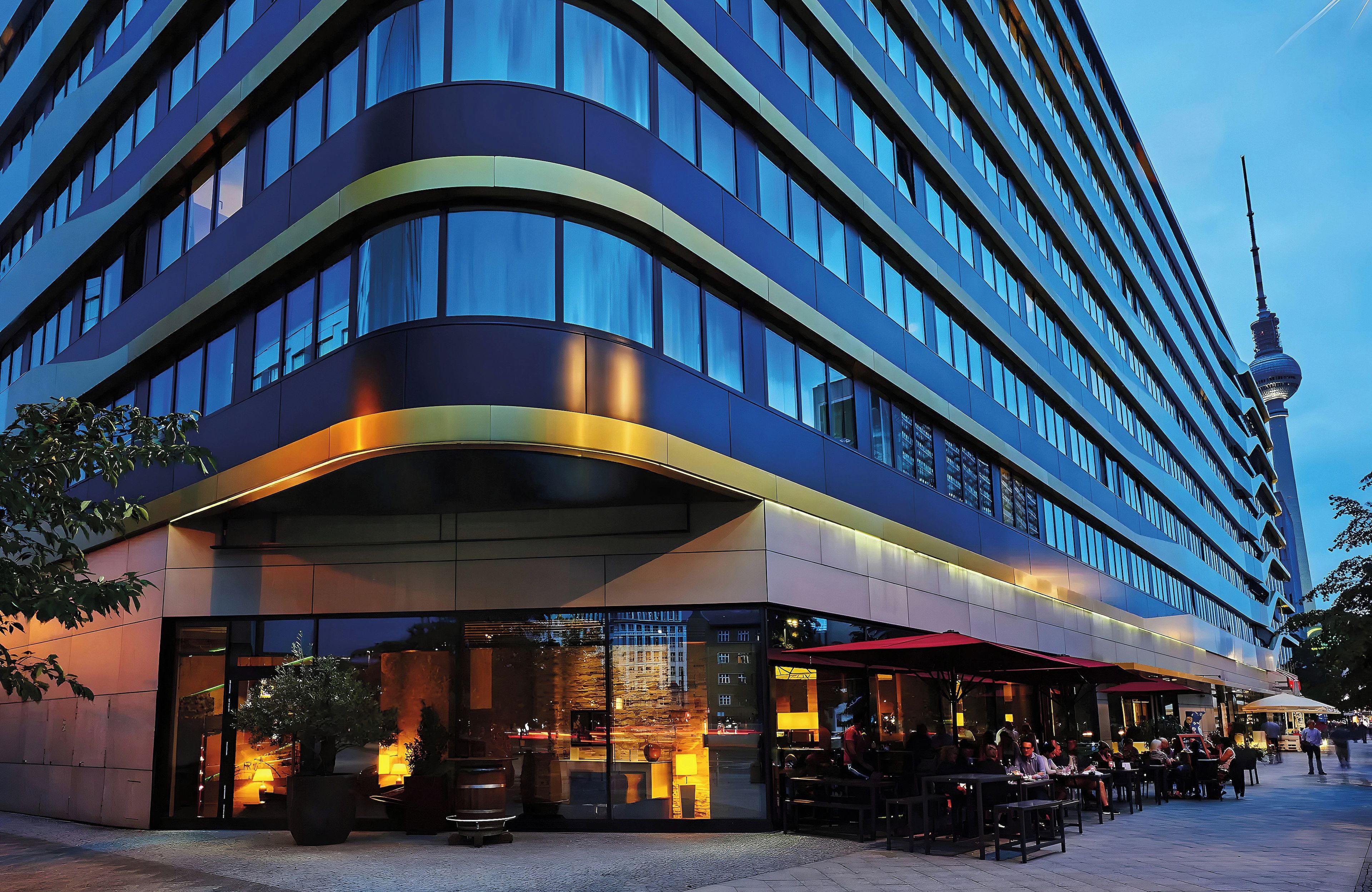 Ein modernes Hotel mit einer geschwungenen Fassade, großen Fenstern und einem Essbereich mit Außenplätzen.
