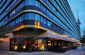 Un hotel moderno con fachada curva, grandes ventanales y un comedor con mesas al aire libre.