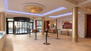 Eine geräumige Lobby mit einer Doppeltür, einem Empfangstresen und einer Sitzecke mit Tischen und Stühlen.