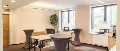 A modern conference room with a round table, two side tables, a potted plant, and large windows.