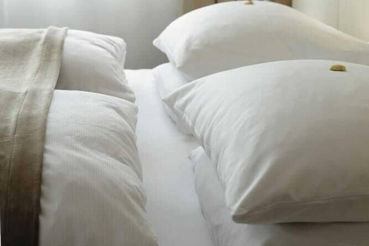 Quarto de hotel com cama, roupa de cama branca, cabeceira e janela com cortinas.